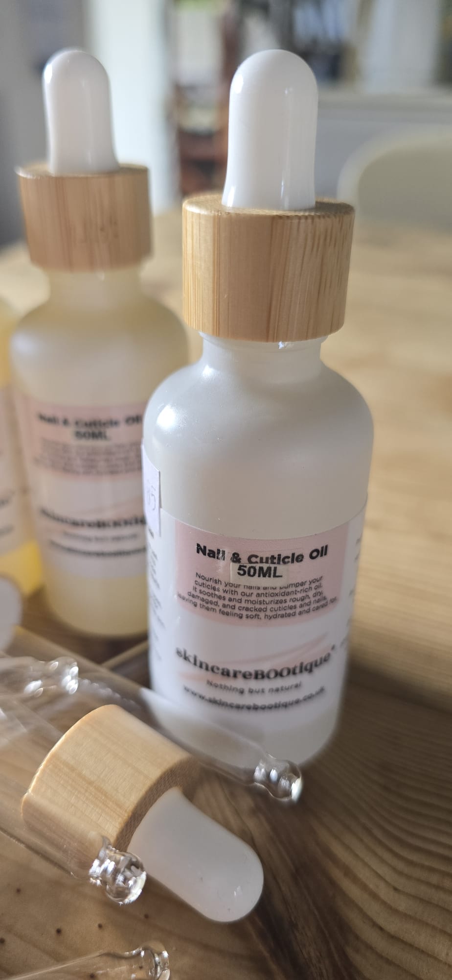 Bottle of skincareBOOtique 'Nail & Cuticle Oil' with wooden dropper on a wooden surface.