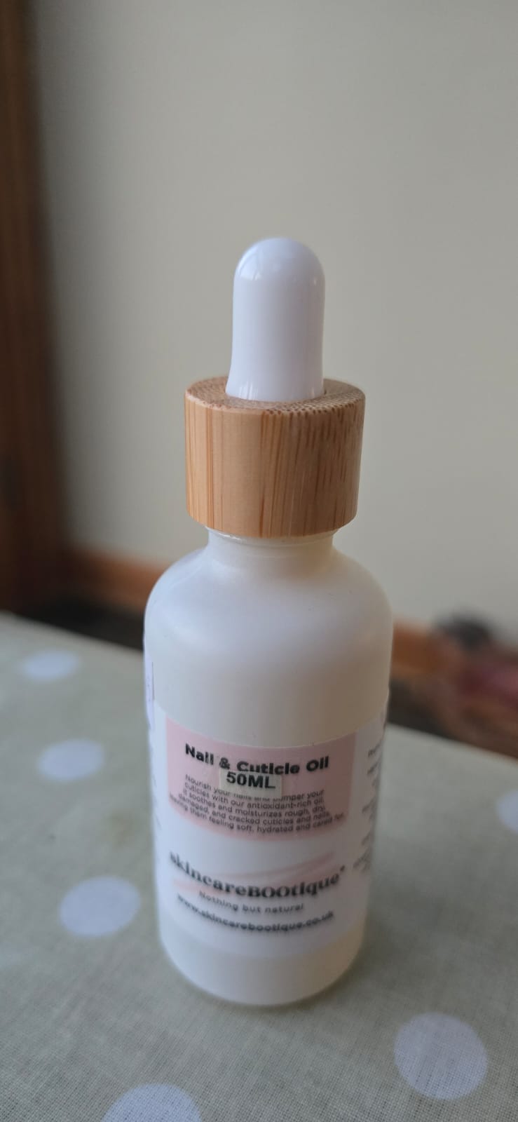 SkincareBOOtique Nail Oil dropper bottle with wooden cap on a polka dot surface