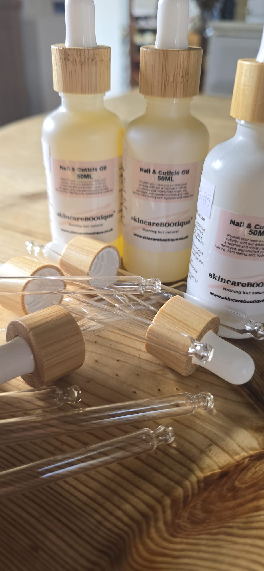 SkincareBOOtique nail and cuticle oil bottles with droppers on a wooden surface