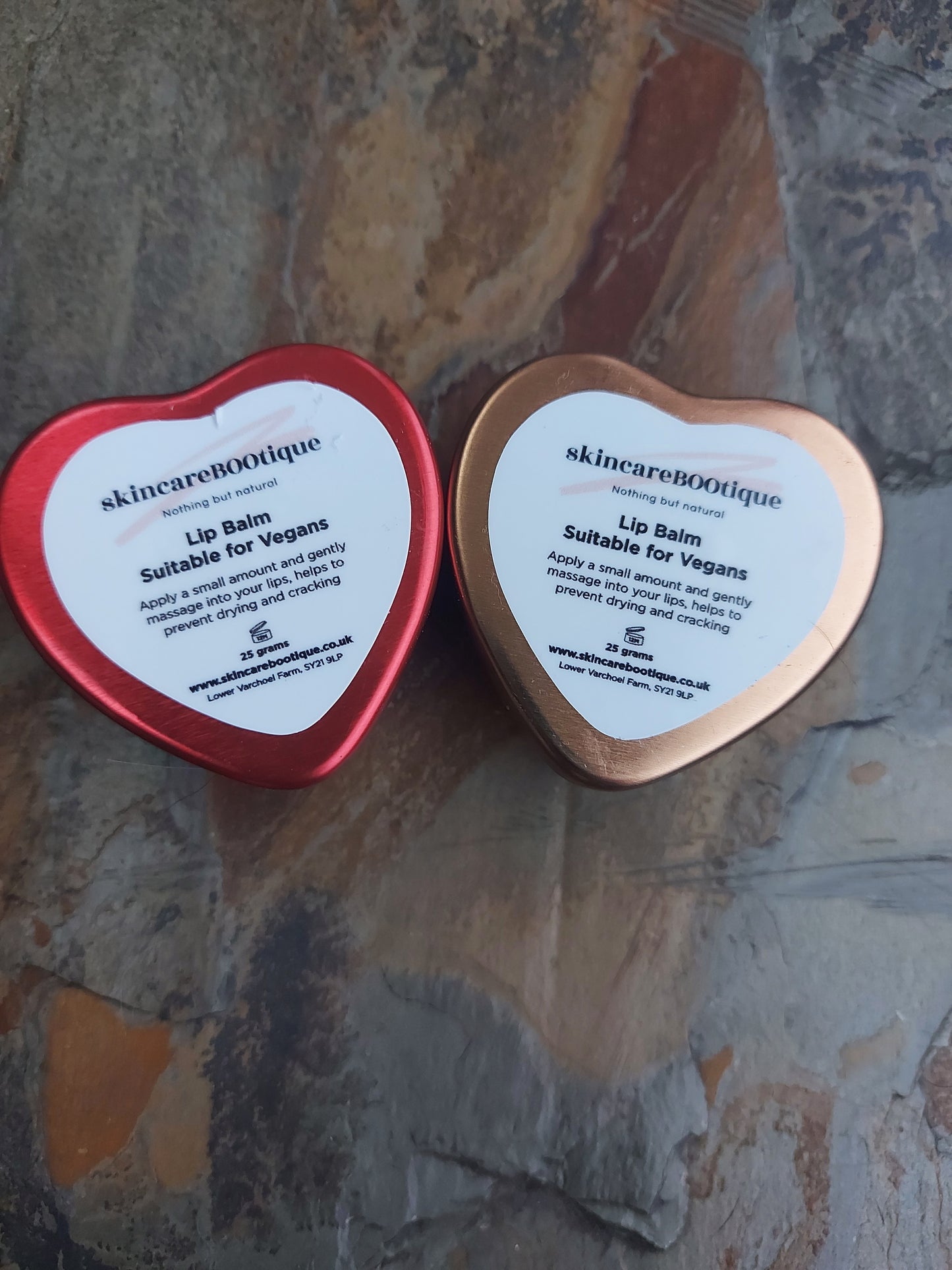 Two heart-shaped lip balm containers from skincareBOOtique on a textured surface.