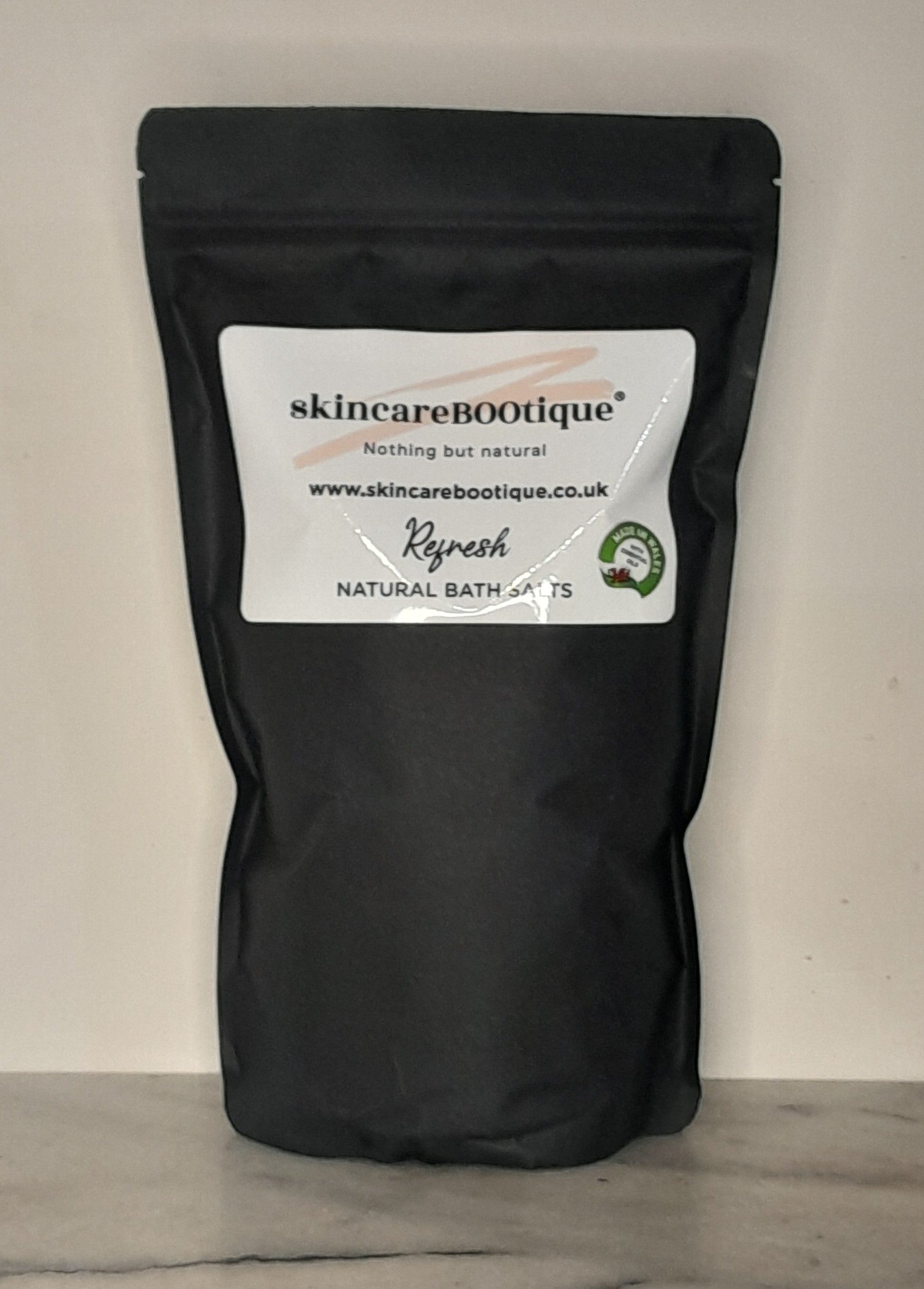 Black bag with skincareBOOtique Refresh Natural Bath saltslabel on a neutral background
